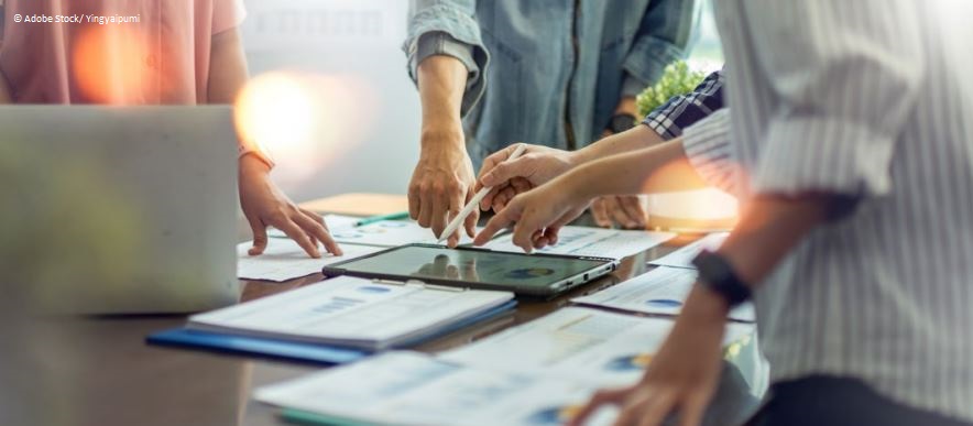 Neue digitale Unternehmenskultur und New Leadership 2 Vier Personen zeigen auf ein Tablet, das auf dem Tisch liegt